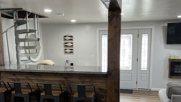 A modern kitchen with a bar area, wooden flooring, and a staircase.