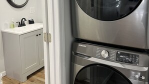 A laundry room with two stacked Samsung washing machines, a mirror, and a white sink with toiletries.