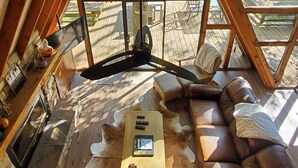 Une pièce aménagée dans les combles, avec un plafond en pente, des poutres en bois, une grande fenêtre, un canapé en cuir, une table basse et une cheminée.