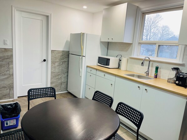 A compact kitchen with a refrigerator, microwave, sink, and a dining area with chairs and a table. - 5 min walk to Clifton, Casino & FALLS (Niagara Falls)
