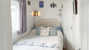 Ein ordentlich eingerichtetes Schlafzimmer mit Bett, Fenster mit Vorhängen, einer Wandablage mit Lampe und einem Willkommensschild.