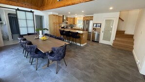 Une cuisine spacieuse équipée d’appareils modernes, un coin repas avec une grande table et des chaises, et un escalier menant à l’étage supérieur.