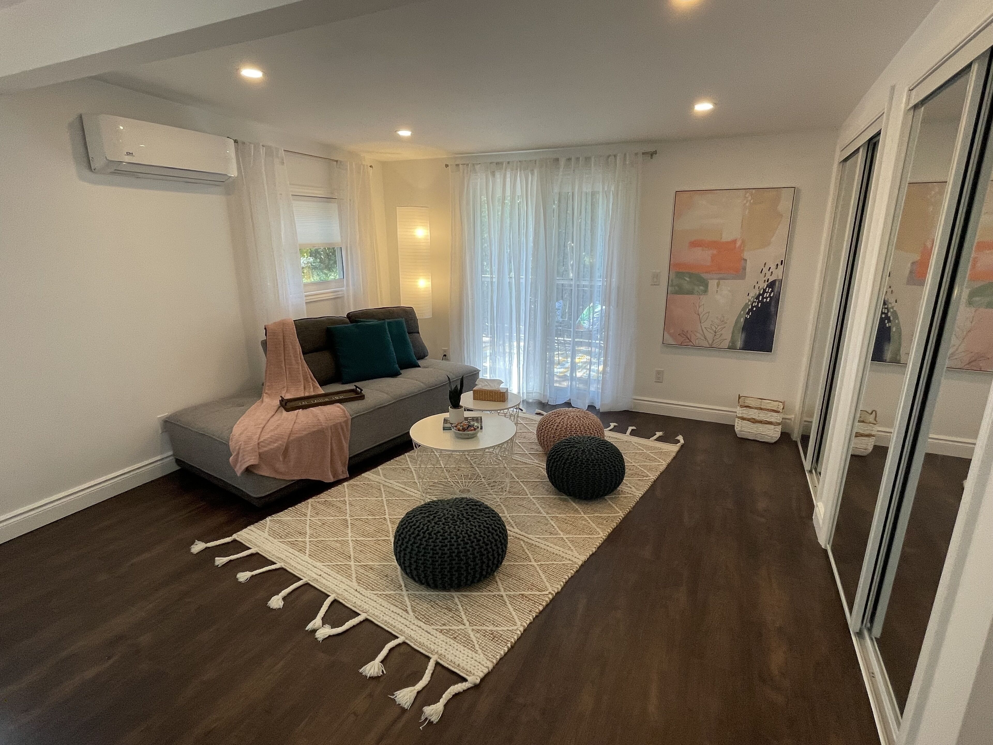 A modern living room with a grey sofa, a coffee table, and a large window with sheer curtains.