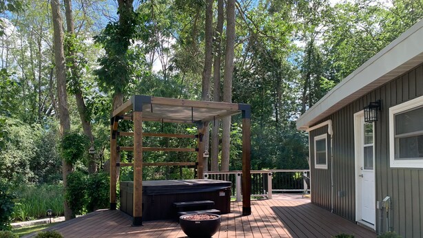 Une terrasse en bois agrémentée d’une pergola, d’un foyer extérieur et d’un petit bâtiment doté d’une porte et de fenêtres.