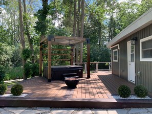 Eine Holzterrasse mit einer Pergola, einer Feuerstelle und einem kleinen Gebäude mit Tür und Fenstern.