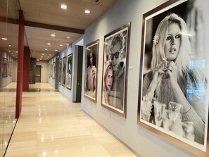 A corridor with framed artwork on the walls, a polished floor, and a red pillar.