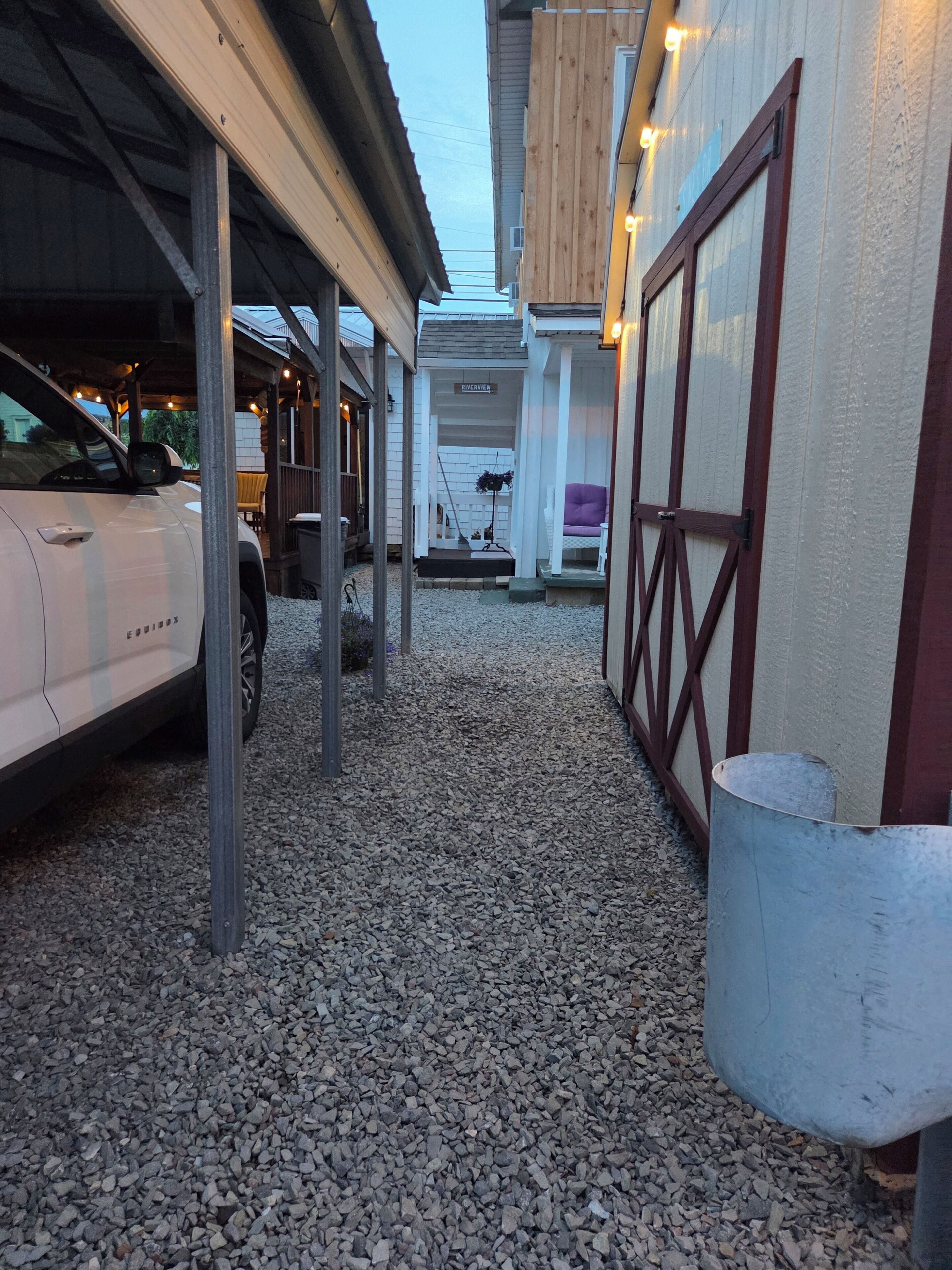 Un camino de grava que conduce a un edificio con zona de estacionamiento techada y un letrero que dice 'RIVERVIEW'.