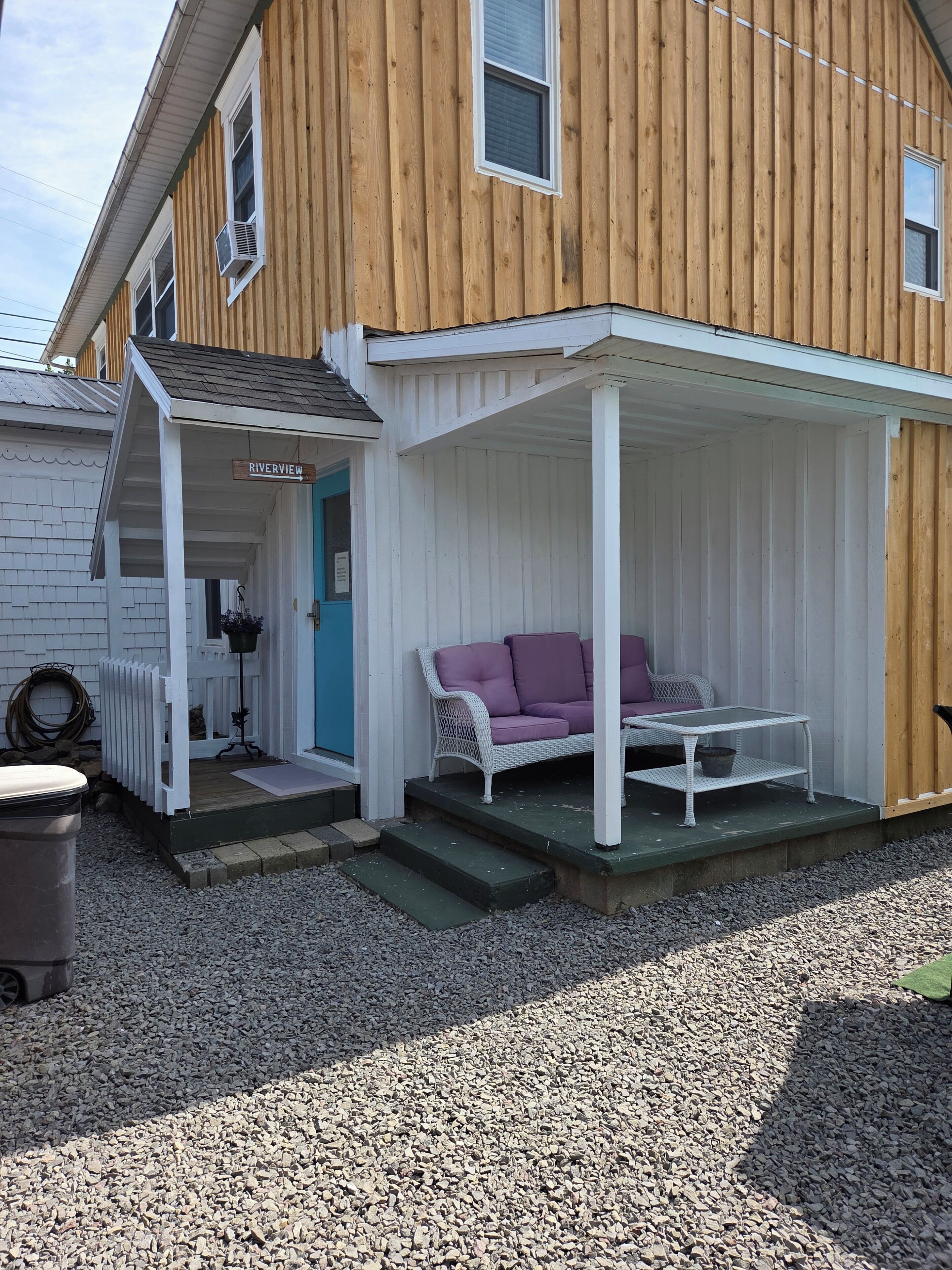 Une maison en bois avec un porche, une clôture blanche, un canapé violet et une petite table.