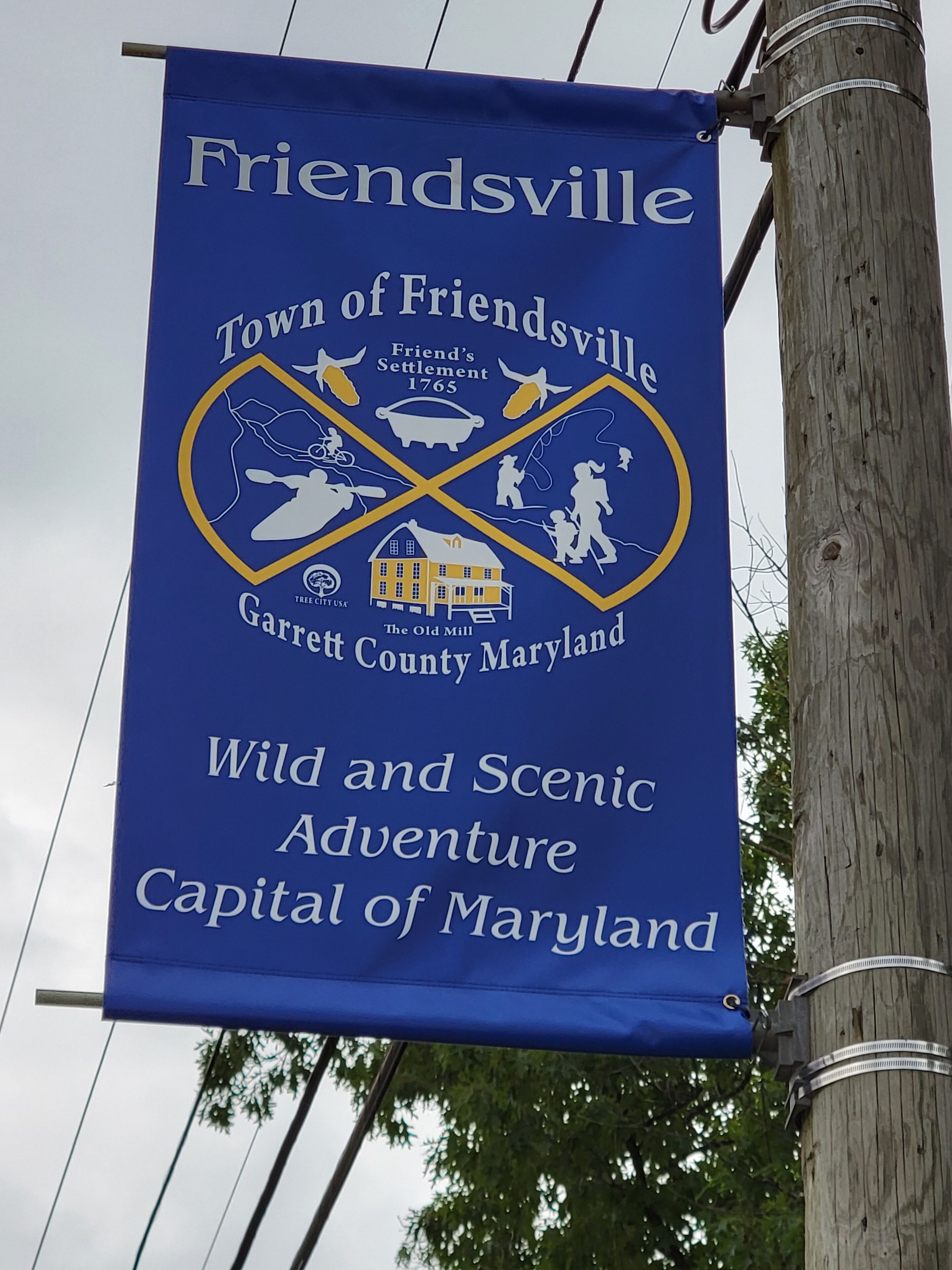 Een blauwe banner met witte tekst die Friendsville promoot als de Stad van Friendsville, Garrett County, Maryland, en als hoofdstad van Maryland, met de nadruk op avontuurlijke en pittoreske attracties.