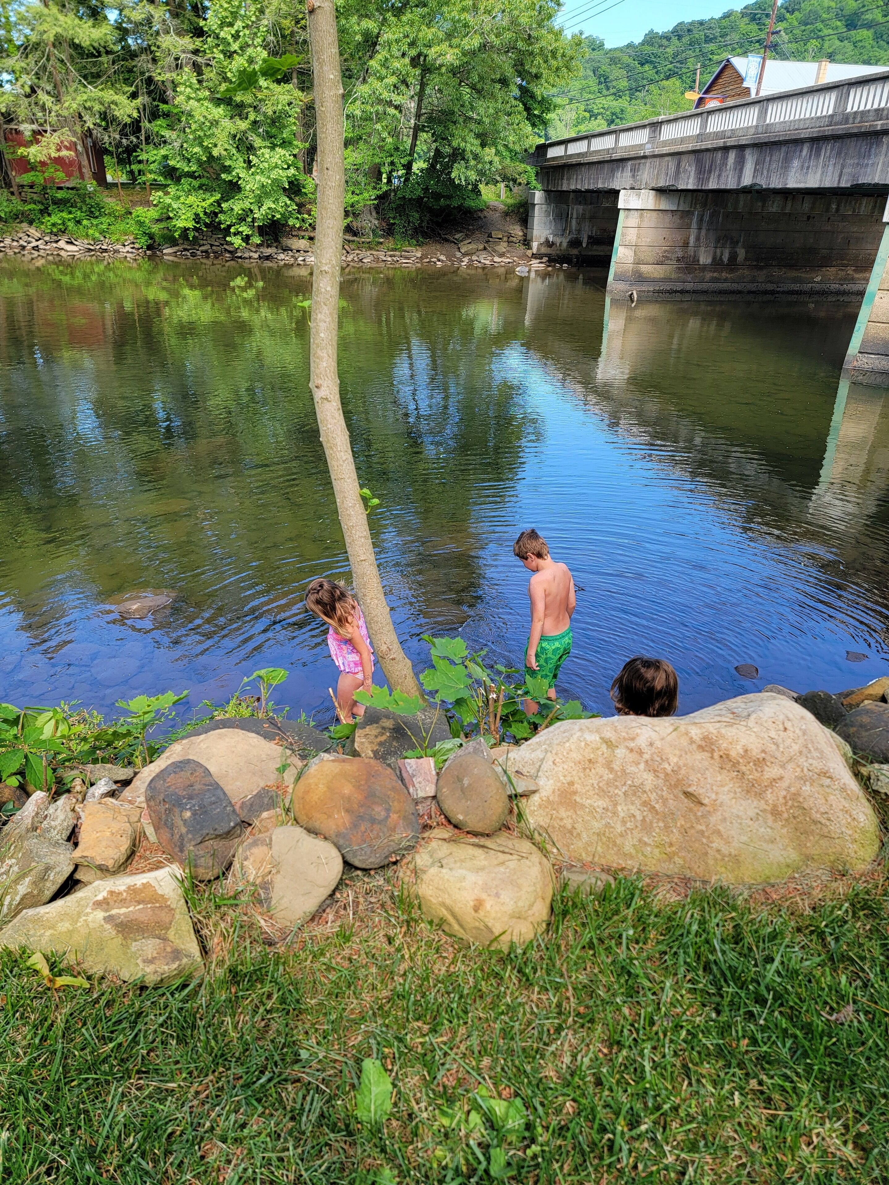 A natural setting with a bridge, a calm river, and a grassy area with rocks.