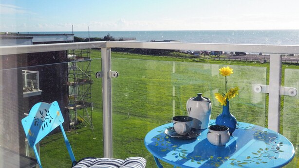 A balcony with a clear view of the sea, a table with a vase and teapots, and a chair. - 2 bedroom accommodation in Bexhill On Sea (Bexhill On Sea)