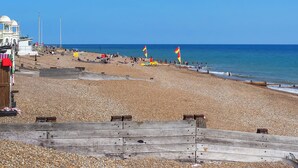 A pebbled beach with a wooden walkway, a white building, and a flag on the right. - 2 bedroom accommodation in Bexhill On Sea (Bexhill On Sea)