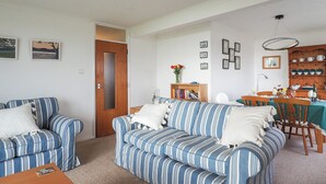 A living room with striped sofas, a wooden door, a bookshelf, and a dining area with a table and chairs. - 2 bedroom accommodation in Bexhill On Sea (Bexhill On Sea)