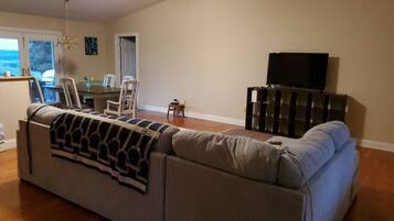 A living room with a large gray sectional sofa, a television on a stand, and a dining area with chairs and a table.