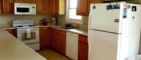 A compact kitchen with wooden cabinets, a microwave, an oven, a dishwasher, and a refrigerator.