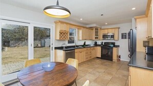A modern kitchen with wooden cabinets, a black countertop, and a dining area with a round table and chairs. - Cozy House less than two miles from Ocean Beaches (Hampton Bays)
