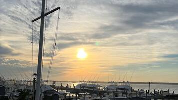 A flagpole with an American flag, a marina with boats, and a sunset in the background.