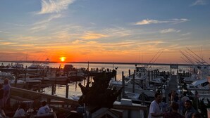 A marina at sunset with boats docked, a docked boat in the foreground, and people gathered on the dock. - Cozy House less than two miles from Ocean Beaches (Hampton Bays)