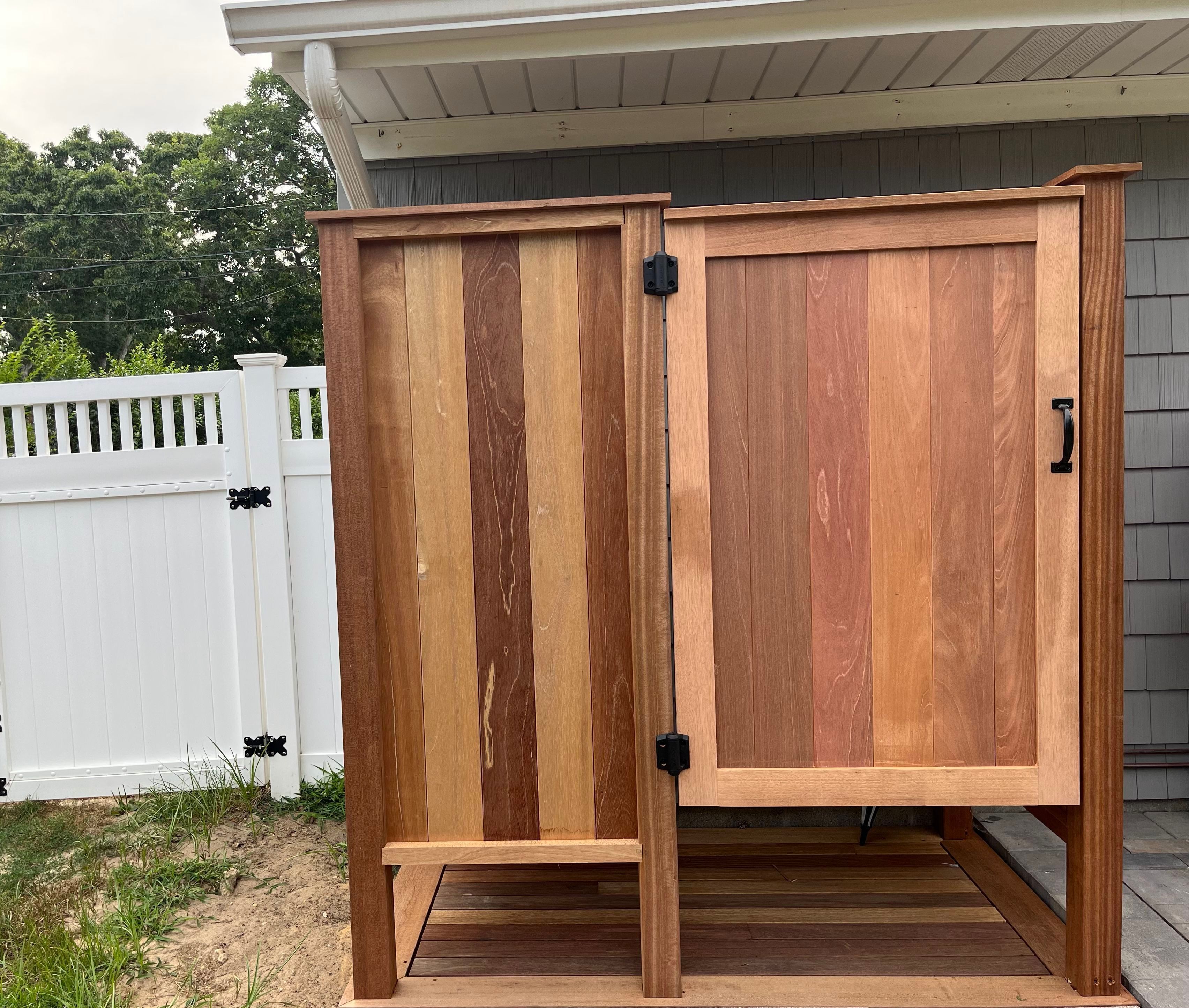 A wooden outdoor storage cabinet with a hinged door and a small step for access.