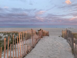 Un sentier de sable bordé d’une clôture en bois qui mène à l’océan.