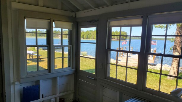 Una stanza con ampie finestre vista lago, un letto con copriletto decorato e un piccolo tavolo con una sedia.
