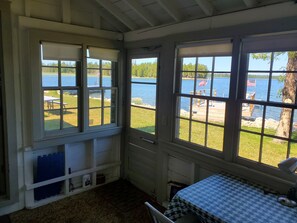 A room with large windows overlooking a lake, a bed with a patterned bedspread, and a small table with a chair. - Rogers Cottage on water front Rowley’s Bay (Ellison Bay)
