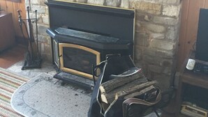 Un camino in pietra con una mensola nera, un ripiano in legno sopra e un quadro con degli anatroccoli appeso al muro.