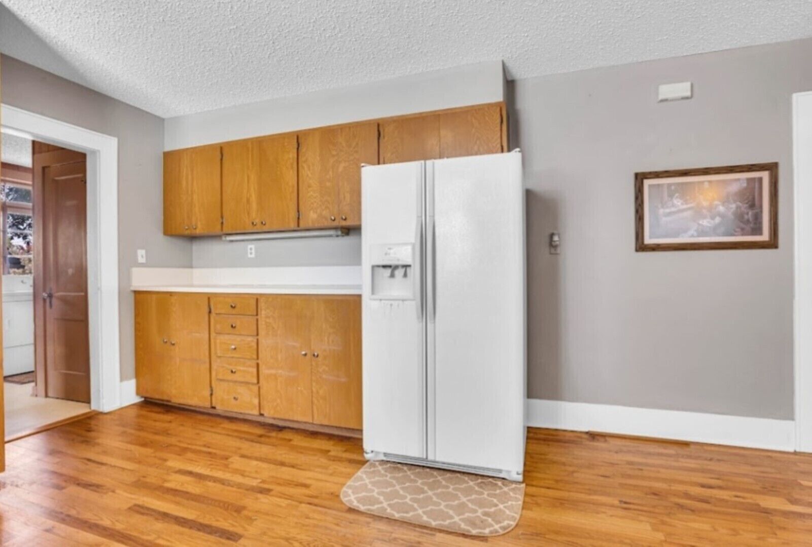 Una cocina con armarios de madera, un refrigerador blanco y una puerta que da a otra habitación.