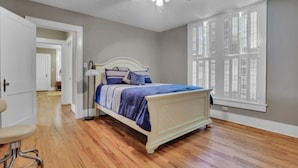 A bedroom with a bed, a ceiling fan, and a window with shutters.
