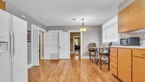 A kitchen with wooden cabinets, a dining table with chairs, and a refrigerator.