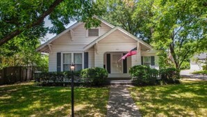 A single-story house with a front porch, a small front yard, and an American flag.