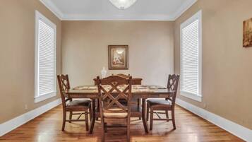 A dining room with a wooden table and chairs, a chandelier, and a painting on the wall.