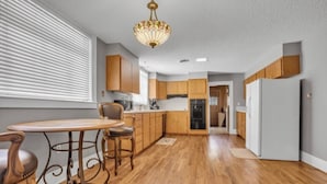 A modern kitchen with wooden cabinets, a dining table with chairs, and a chandelier.