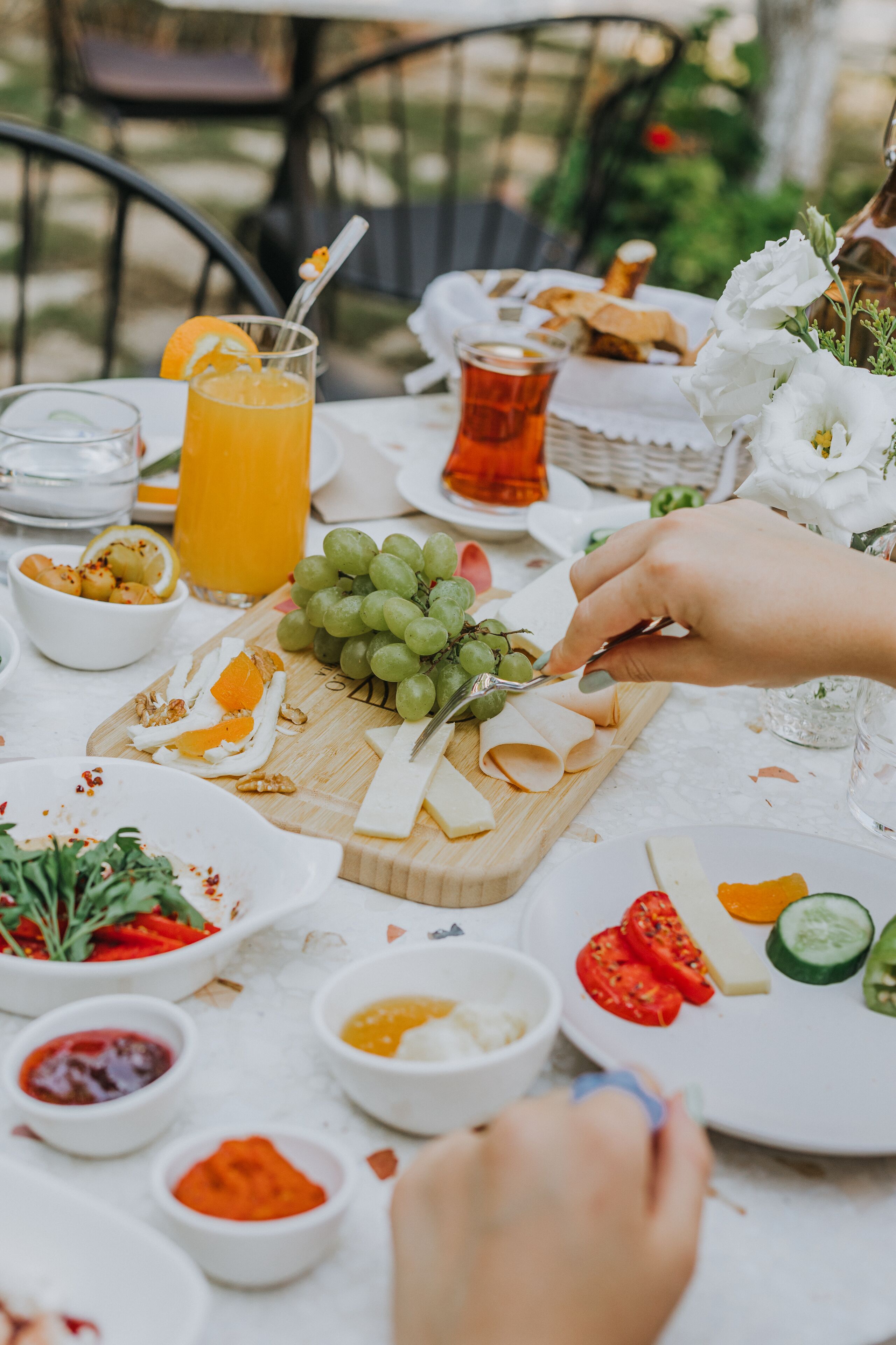 Une table dressée avec divers aliments, notamment du fromage, des raisins et un verre de jus d’orange.