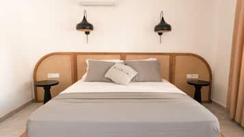 Una cama bien hecha con un edredón gris, dos lámparas de pared negras y una mesita redonda al lado de la cama.