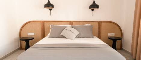 A neatly made bed with a grey bedspread, two black wall-mounted lamps, and a small round table beside the bed.