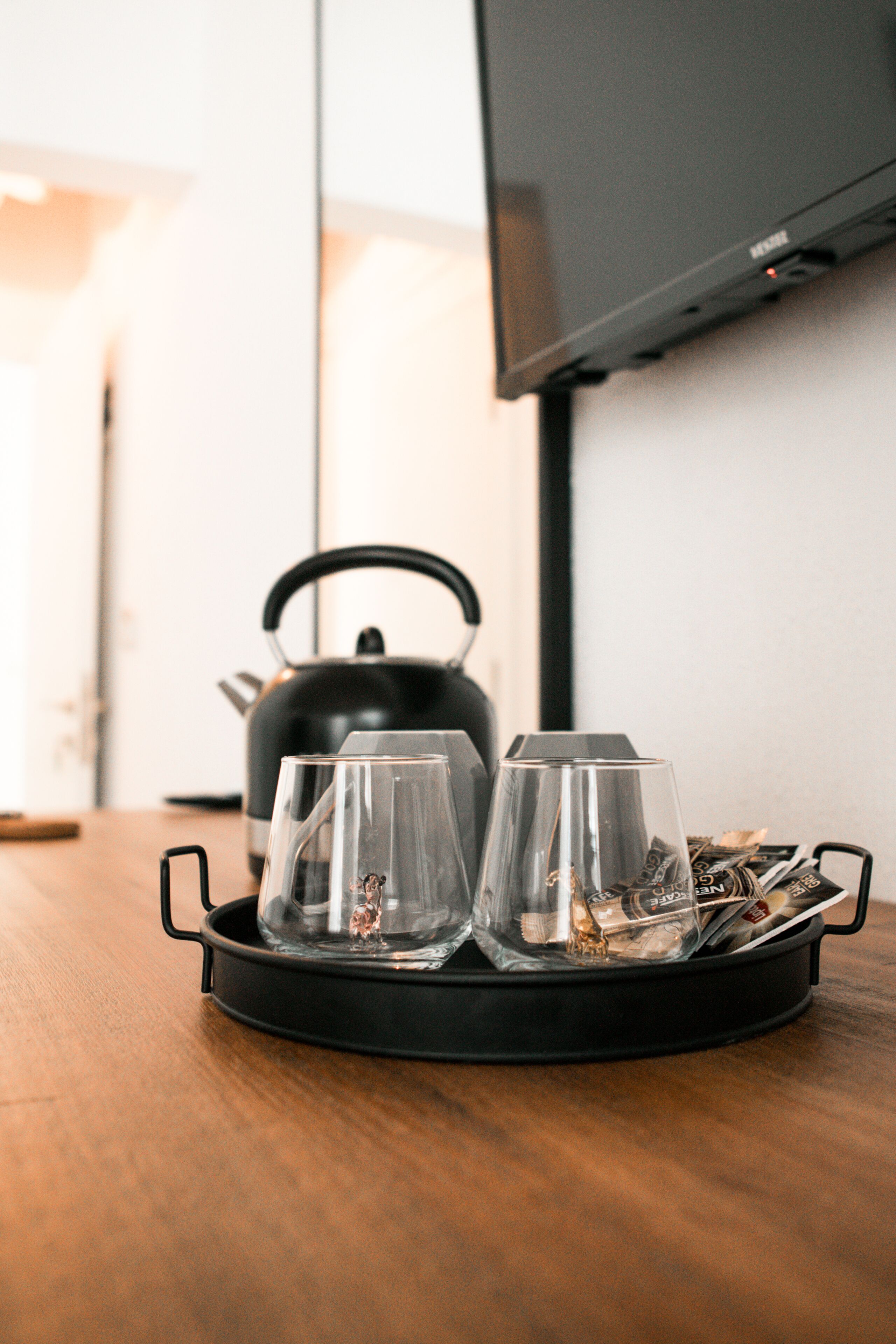 A tray with two glasses and a kettle on a wooden table.