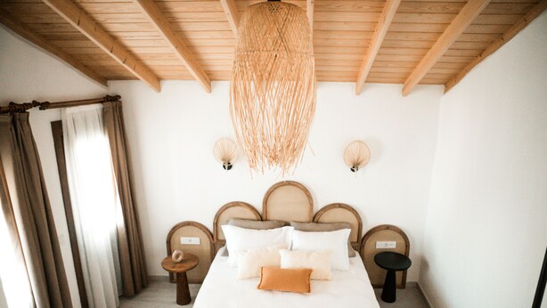 Un dormitorio con techo de madera, una cama con muchas almohadas, dos mesitas de noche y una lámpara colgante.