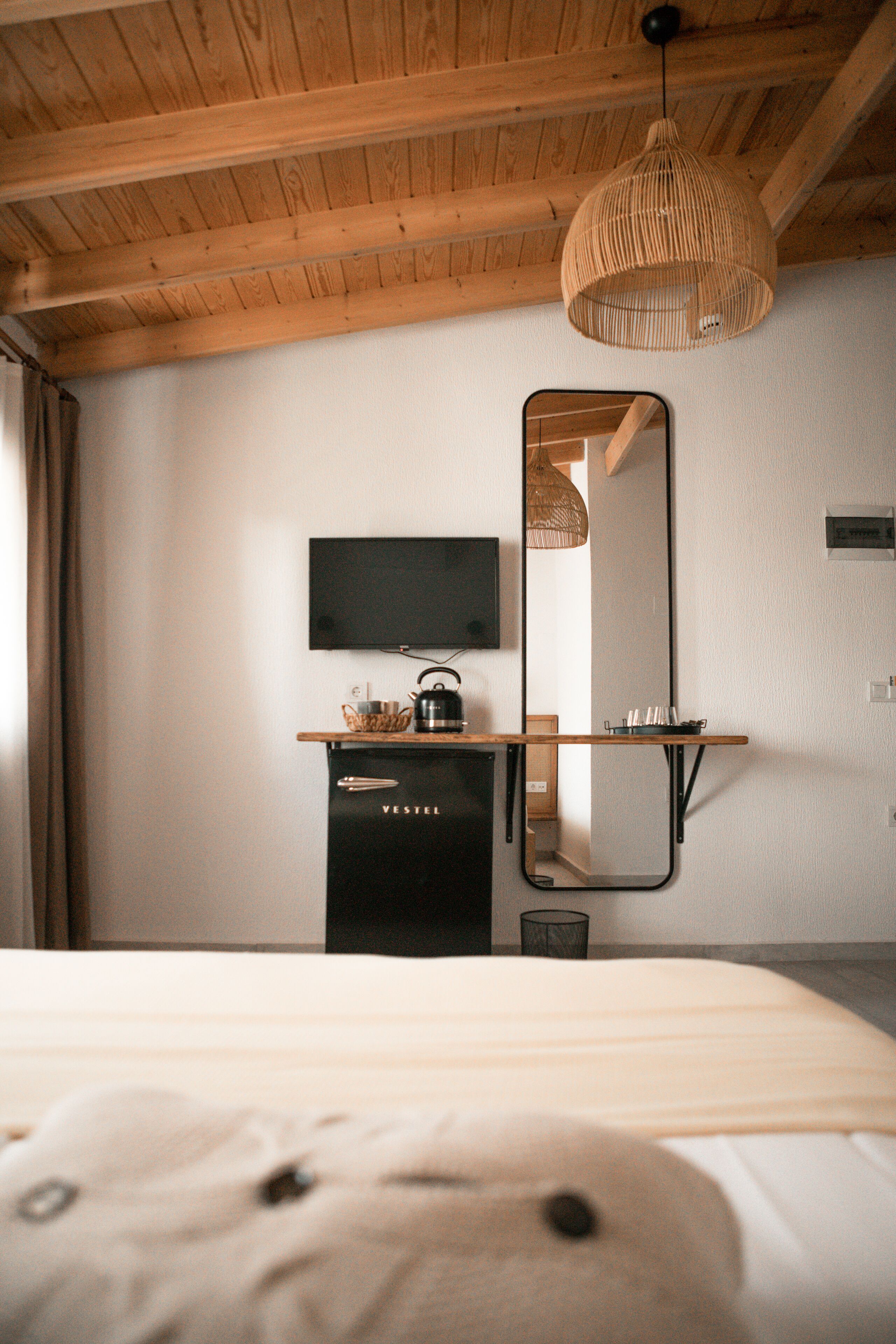 A bedroom with a wooden ceiling, a bed, a dresser, a mirror, and a television on the wall.