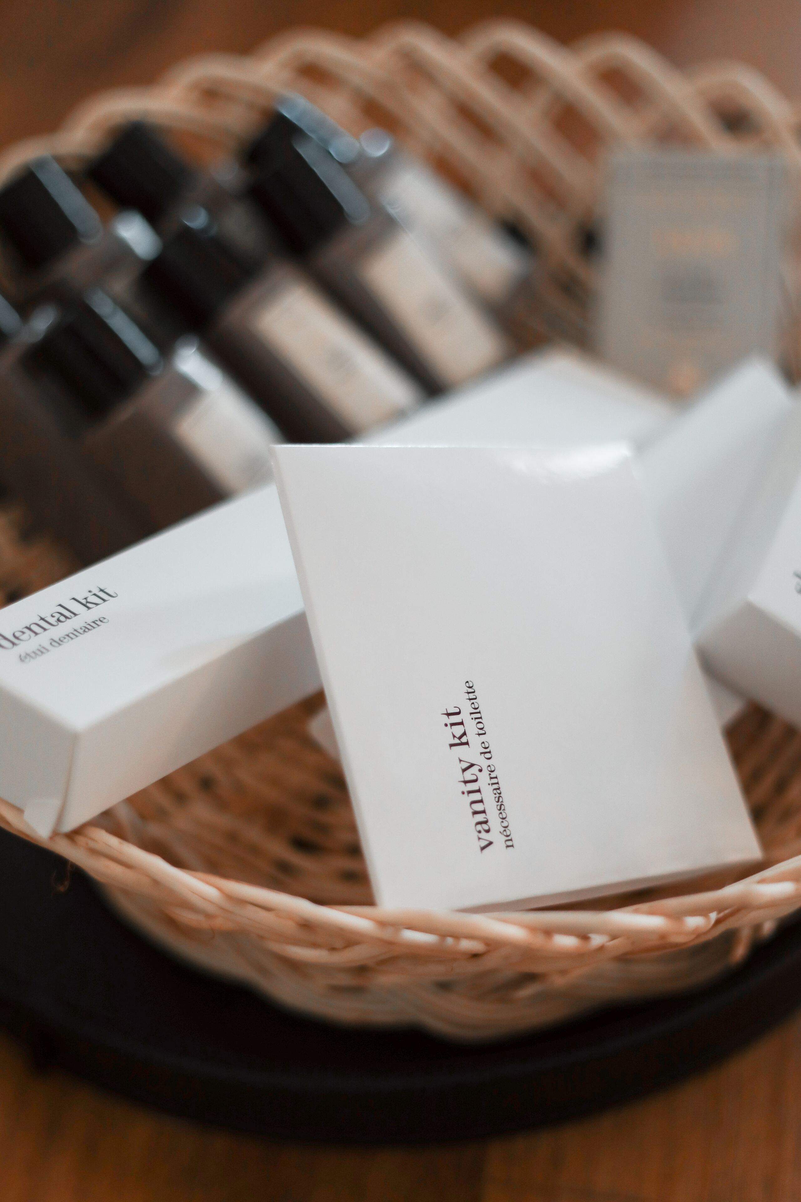 Una cesta de mimbre que contiene varios artículos de tocador, incluyendo botellas y cajas etiquetadas como 'kit de tocador'.