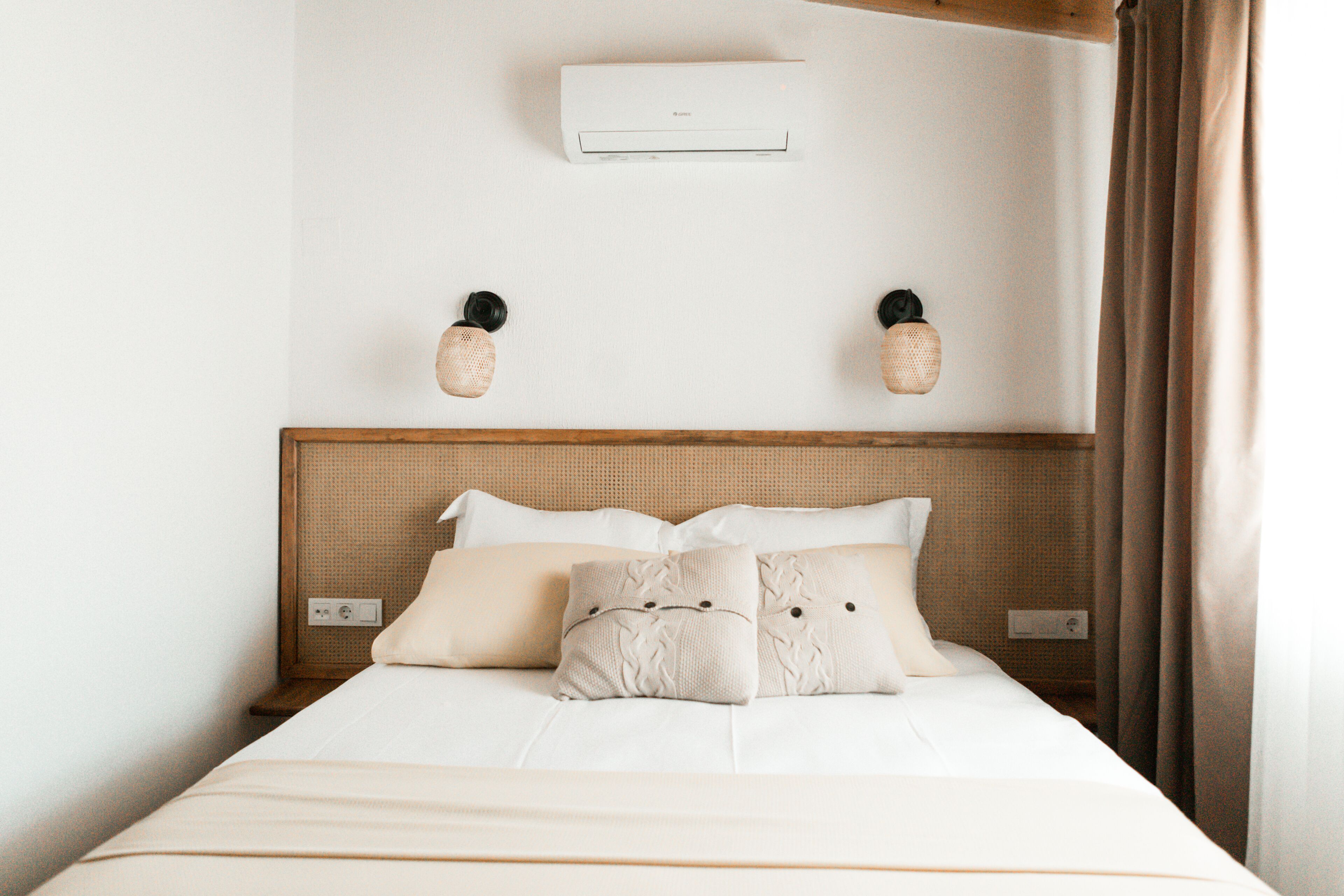 Una cama bien hecha con un cabecero sencillo, un aire acondicionado de pared y dos lámparas de pared.