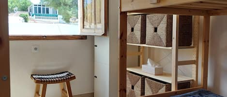 Una cama litera con estantes para guardar cosas, un taburete pequeño y una ventana con persianas.