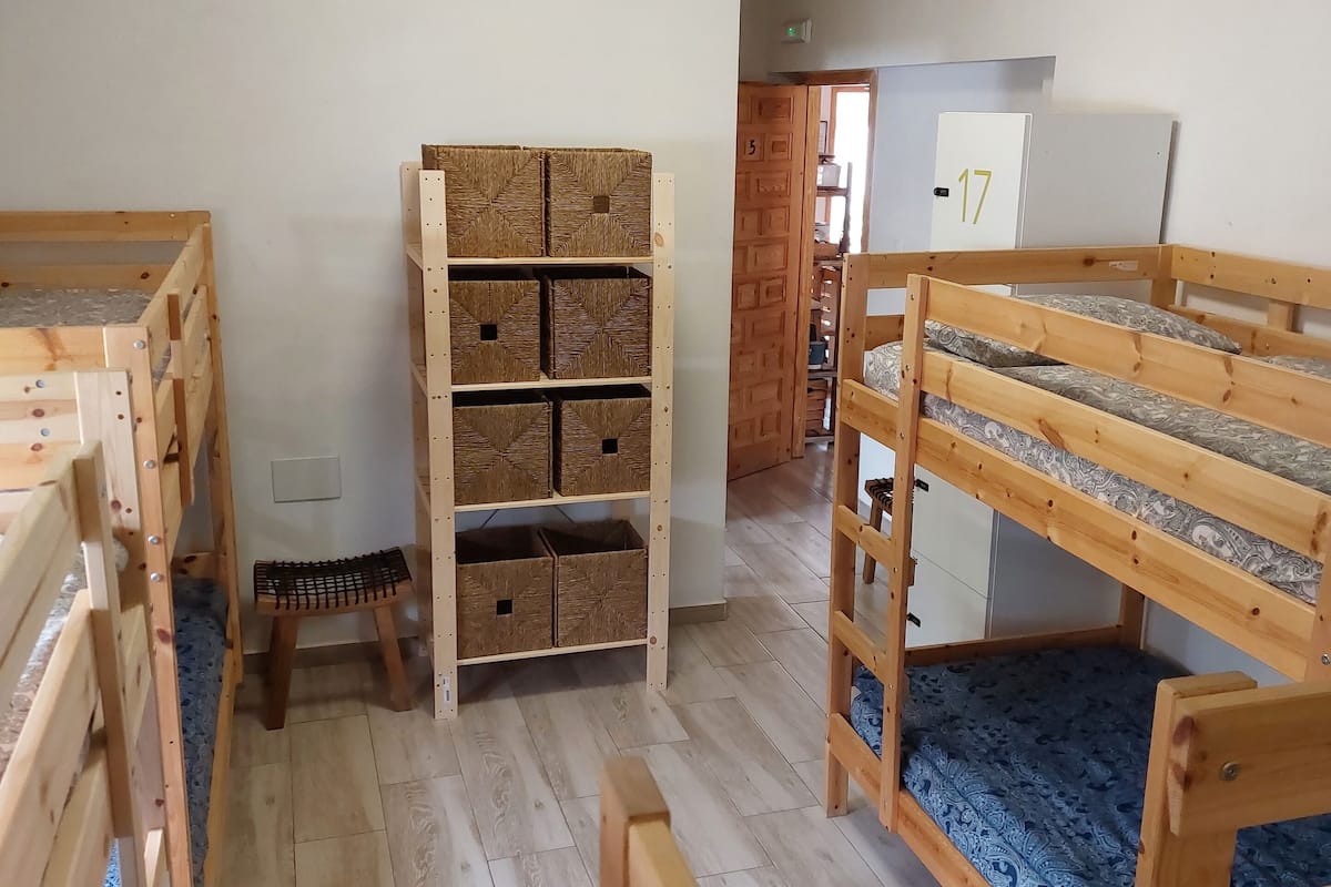 Una habitación con literas, unidades de almacenamiento de madera y un taburete pequeño.