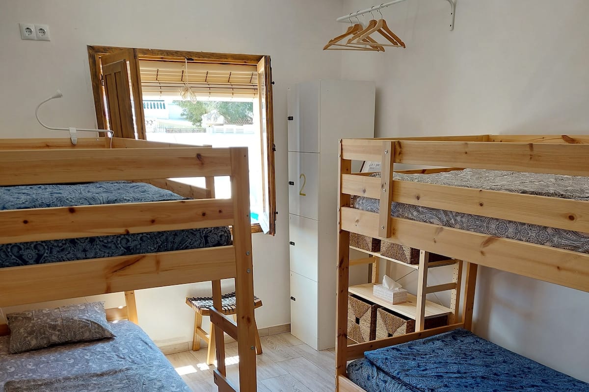 Una habitación con dos literas, un escritorio de madera, un armario y una percha para ropa.