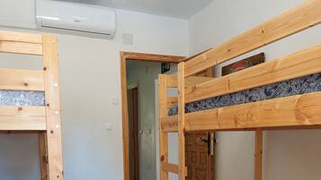 Una habitación con dos literas, un taburete de madera y una puerta que da a otra estancia.