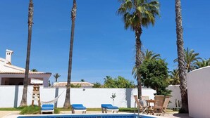 A swimming pool surrounded by palm trees, with lounge chairs and a white building in the background. - ZENIA HOSTEL (Orihuela)