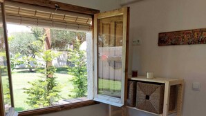 A bedroom with a large window, a bed with blue bedding, a small stool, and a wooden shelf with baskets. - ZENIA HOSTEL (Orihuela)