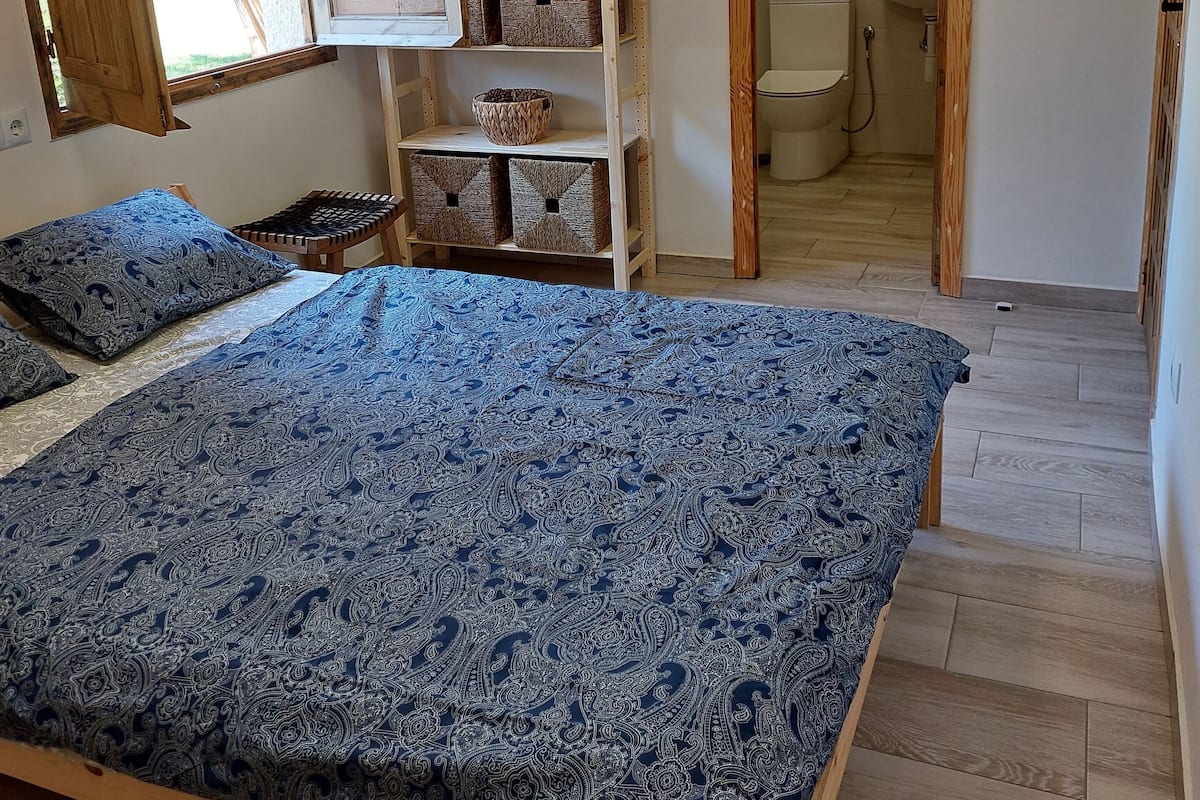 Un dormitorio con cama, estanterías de madera, una ventana con cortinas, aire acondicionado y vistas al baño.