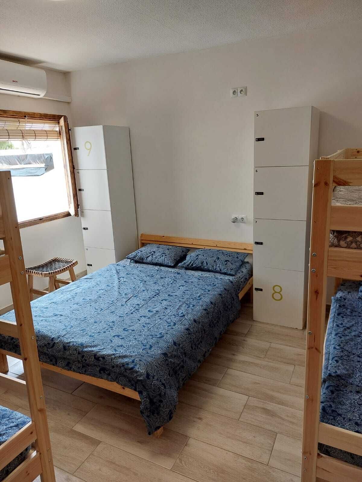 Una habitación tipo dormitorio con una cama litera, una cama individual, un armario y una pequeña mesa.