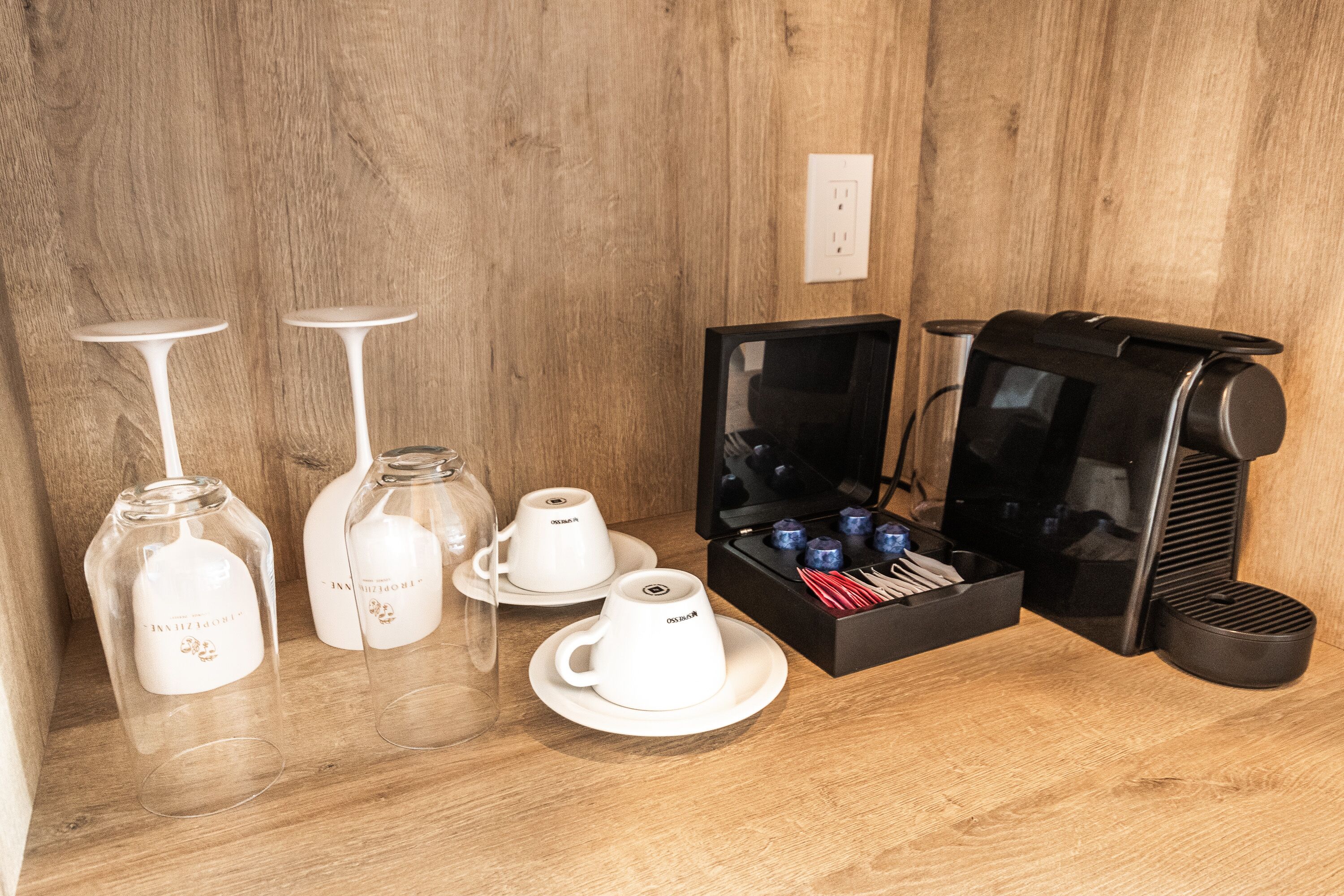A coffee station with a coffee maker, cups, and a tray of utensils.